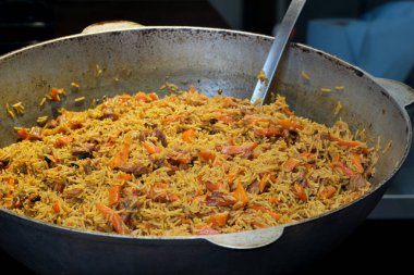 Yumuşak et ve canlı sebzelerle karıştırılmış altın pirinç büyük bir tavada kaynıyor..