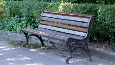 Dayanıklı ahşap bir bank davetkar bir şehir parkında oturur ve ziyaretçileri çağırır..