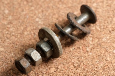 Yaşlanmış metalik cıvatalar ve fındıklar desenli bir yüzeyde duruyor. Çürüme belirtileri gösteriyor..