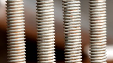 Bir atölyede ahşap bir yüzeye dizilmiş başlıklı metal çubukların yakın çekimi.