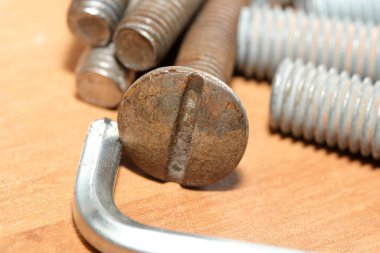 Tahta bir yüzeyde çeşitli vidalarla çevrili paslı bir sürgüye yakın çekim..