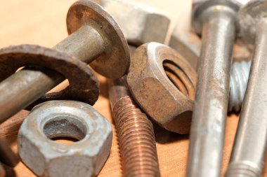 Çeşitli vidalar, cıvatalar ve fındıklar ahşap bir masaya saçılmış, çeşitlilik sergiliyor..