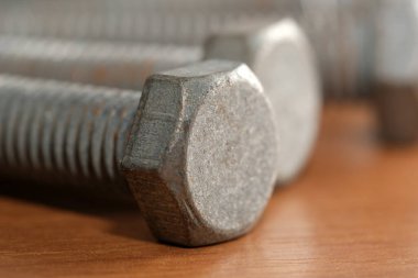 Ahşap bir masanın üzerindeki metalik uğursuz cıvataların yakın çekimi dokularını ve şekillerini vurgular.