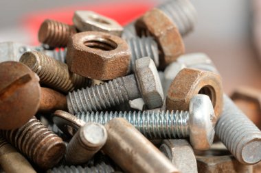 Çeşitli paslı ve parlak cıvatalar, fındıklar ve vidalar tezgahın üzerine saçılmış..