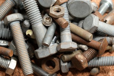 Çeşitli cıvatalar, fındıklar ve vidalar kumlu bir tezgahta karışıyor..