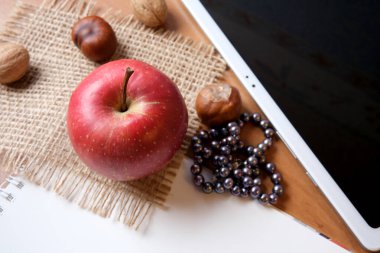 A vibrant red apple rests on burlap fabric beside scattered nuts and beads.