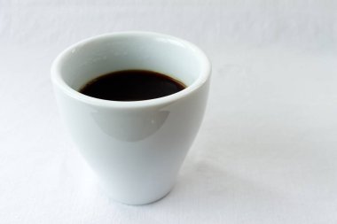 Beyaz seramik fincanın minimalist görüntüsü. Temiz beyaz arka planda sade kahve. Geniş kopya alanı ile kafeler, menüler, bloglar veya sabah ritüelleri, enerji ve iş molaları için idealdir..