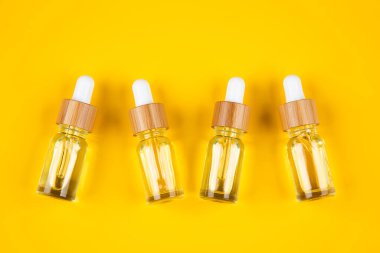 Sarı arka planda, gölgeli serumu ve pipeti olan kozmetik şişeleri..