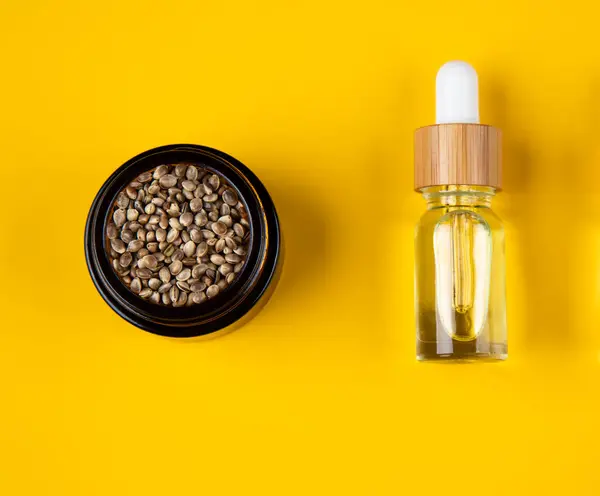 麻油精油与一杯新鲜和麻籽的黄色背景 替代疗法 图库图片
