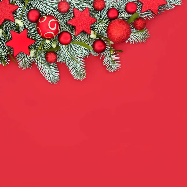 Festive Christmas sparkling background border on red with snow fir, mistletoe and bauble tree decorations. Colourful traditional festive design for Xmas holiday season.