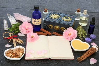 Aphrodisiac love potion recipe ingredients with magic spell notebook with herbs, rose flowers, honey, fertility corn dolly, oil, spring water and quartz crystals. Wiccan occult concoction for lovers.  