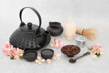 Kukicha twig and apple blossom tea drink. Japanese ceremony with ceramic teapot set, Buddha statue. Good health and inner peace, mindfulness concept. On mottled grey background.
