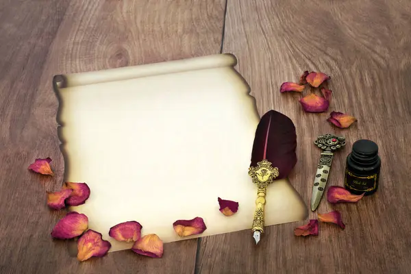 Parchment paper scroll with dried red rose petals and old feather quill pen. Retro writing equipment for love letter for Valentines Day on rustic wood.