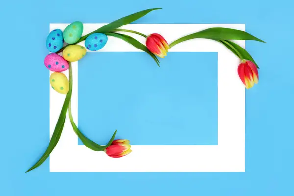 Easter eggs and tulip flowers abstract with white frame on blue background. Minimal floral festive design for the holiday season.