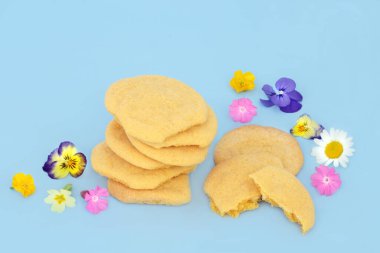 Homemade white chocolate custard cookies with scattered Spring flowers and wildflowers on blue background. Natural comfort food floral nature composition. clipart