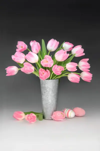 粉色复活节彩蛋和郁金香花仍然在金属花瓶的梯度黑色白色背景的生活安排 复活节花卉自然设计 图库图片