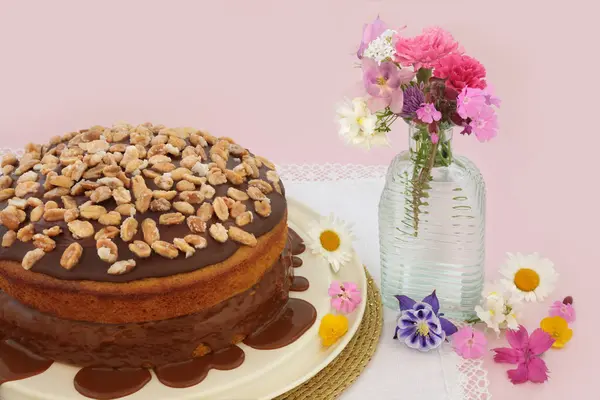 自家製ピーナッツケーキと夏の花とピンクの背景にピーナッツで飾られたキャラメルソース おいしいアフタヌーンティーフローラル構成 — ストック写真