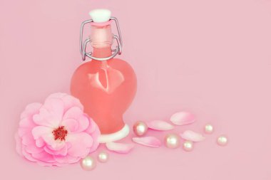 Gül çiçeği kalp şeklindeki parfüm şişesi pembe arka planda inci yapraklı. Sevgililer Günü, doğum günü, Anneler Günü için çiçek kokulu doğal bir hediye..