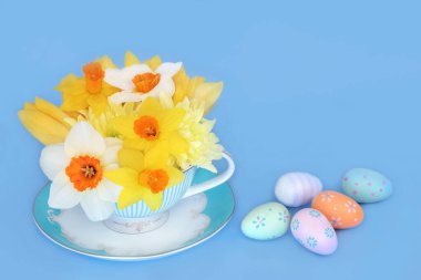 Süslü çikolatalı yumurtalarla porselen çay fincanında gerçek üstü Paskalya bahar çiçekleri. Mavi arka planda soyut tatil mevsimsel kompozisyonu.