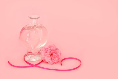 Pembe arka planda kalp şeklinde bir şişede gül çiçeği parfümü. Sevgililer Günü için kadınsı kokulu hediye, doğum günü, yıldönümü, düğün, Anneler Günü.