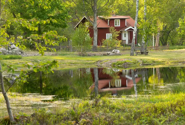 春にスウェーデンの小さな池を持つ伝統的な赤い木製の家 家と周辺の新緑が池に映し出される ストック画像