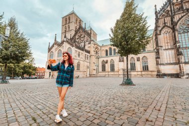 Mutlu turist kız St. Paulus Dom Katedrali 'ni ziyaret ederken selfie çekiyor ve Almanya' nın Munster kentindeki eski kasaba mimari binalarına hayran kalıyor.