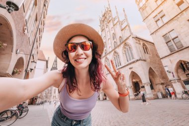 Mutlu turist kız Prinzipalmarkt caddesini ziyaret ederken selfie çekiyor ve Almanya 'nın Munster kentindeki eski kasaba mimari binalarına hayran kalıyor.