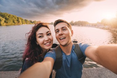 Birbirine aşık bir çift ya da sadece arkadaş öğrenciler şehir parkında gün batımı manzaralı bir selfie çekiyorlar. Tatil, eğitim ve ilişki kavramı