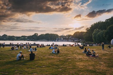 25 Temmuz 2022, Munster, Almanya: Munster şehir parkında dinlenen ve Aasee Gölü üzerinde gün batımını izleyen insanlar