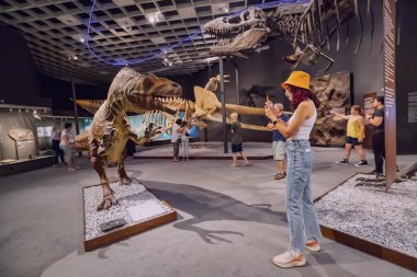 26 Temmuz 2022, Munster Doğal Tarih Müzesi, Almanya: Korkunç dinozor iskeletleri sergisinde elinde akıllı telefon uygulaması rehberi olan ziyaretçi kız
