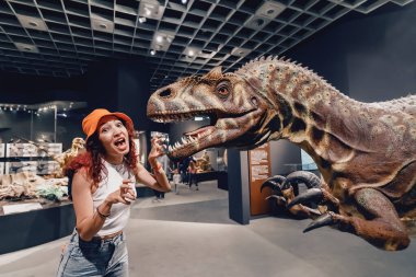 26 Temmuz 2022, Munster Doğal Tarih Müzesi, Almanya: Dinazor sergisine bir kız ziyaretçi etrafta geziyor ve yırtıcıyı korkutmaya çalışıyor
