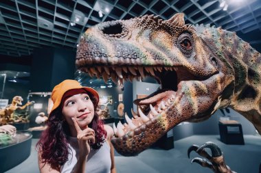 26 Temmuz 2022, Munster, Almanya: Komik turist kız veya paleontolog öğrenci Doğa Tarihi Müzesi 'ndeki bir dinozorun büyük dişleriyle açık çeneye bakar