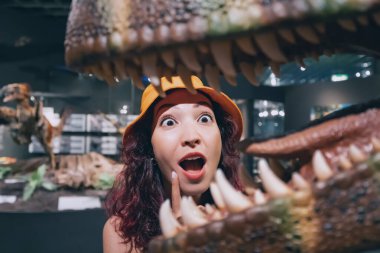 26 Temmuz 2022, Munster, Almanya: Komik turist kız veya paleontolog öğrenci Doğa Tarihi Müzesi 'ndeki bir dinozorun büyük dişleriyle açık çeneye bakar