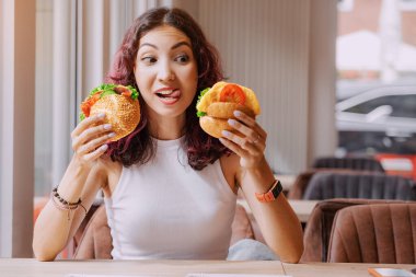 Asyalı mutlu bir kız ve iki hamburger ya da sandviç arasında seçim yapıyor. Biri vejetaryen, diğeri etli.