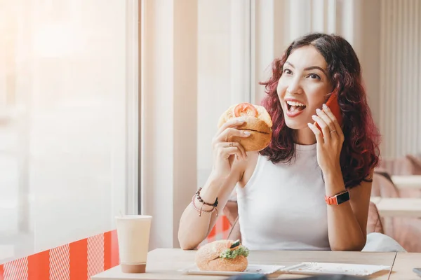 Женщина Ест Гамбургер Кафе Быстрого Питания Разговаривает Другом Телефону — стоковое фото