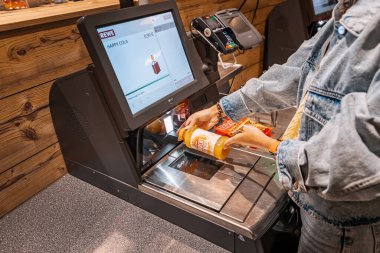 30 Temmuz 2022, Köln, Almanya: Rewe süpermarketindeki otomatik self-servis kontrol terminalinde kız müşteri tarayıcıları ve bir şişe juce için ödeme