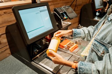 Bir kız, otomatik self-servis kontrol terminalinde bir süpermarketten bir şişe meyve suyu alıyor ve parasını ödüyor.