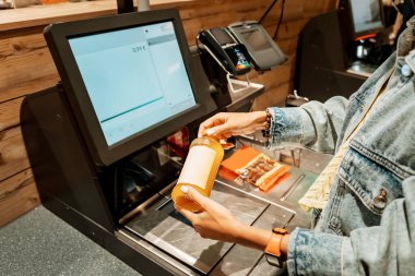 A girl customer scanns and pays for bottle of juice from a supermarket in an automated self-service checkout terminal clipart