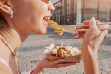Cologne City Caddesi 'ndeki yemek çubuklarını kullanarak paket kutusundan börek yiyen neşeli kız. Fast food ve Asya mutfağı.