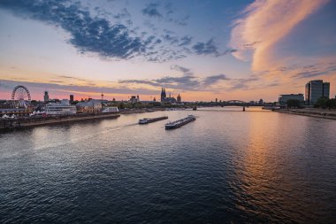 30 Temmuz 2022, Köln, Almanya: Koln şehrinin panoramik manzarası, Ren Nehri, köprüler ve çeşitli mavnalar ve gemiler günbatımında.