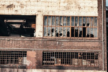 Endüstriyel bölgede, camları taşlardan, kurşunlardan ve kırıklarından kırılmış bir bina. Askeri çatışma, gettolar ve kırık camların sosyal teorisi.