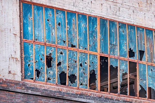 Endüstriyel bölgede, camları taşlardan, kurşunlardan ve kırıklarından kırılmış bir bina. Askeri çatışma, gettolar ve kırık camların sosyal teorisi.