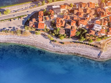 Arka planda eski bir tatil köyü ve mavi deniz ya da göl manzarası var.