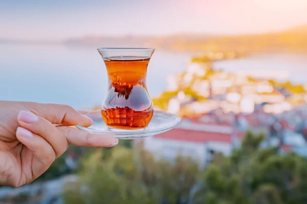 stock image Delicious and fragrant Turkish tea in a traditional authentic bardak glass in the hand of a tourist against the backdrop of a resort town