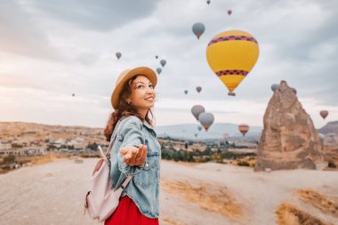 Kapadokya, Türkiye 'deki maceraya katılın. Genç bir kadın arka planda yükselen sıcak hava balonlarıyla beni takip ediyor..
