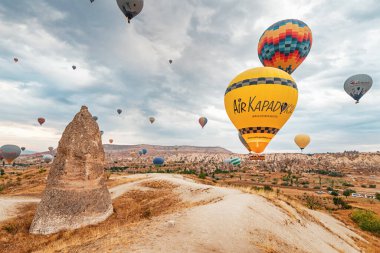 13 Eylül 2022, Kapadokya, Türkiye: Sıcak hava balonları baş döndürücü kaya oluşumları ve bulutlu gökyüzüne karşı zahmetsizce yüzerler..