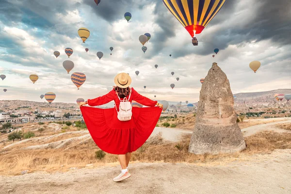 In the beautiful landscape of Cappadocia, the girl in her flirty dress finds joy in the sight of the air balloons, her dreams of travel conjured in the sky