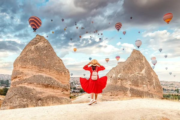She stands in the warm summer air, dress fluttering in the breeze, dreaming of the wide world as she watches the bright balloons drift away over Cappadocia, Turkey