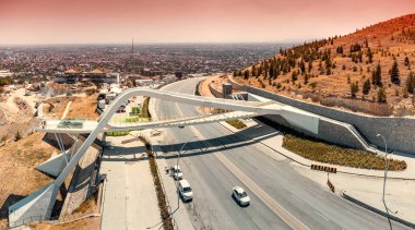 Hızlı ve yoğun bir otoyolda arabalarla güvenli bir geçiş için yaya köprüsünün havadan görüntüsü.
