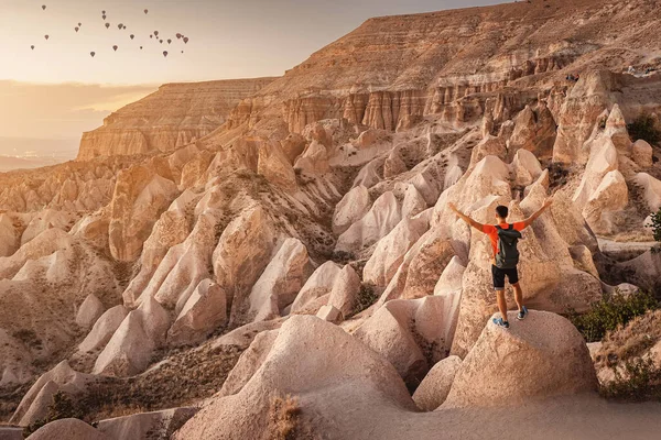 男性旅行者欣赏卡帕多西亚 土尔其耶不同锥形的地质构造 以及日落时背景中的一组飞行气球 — 图库照片